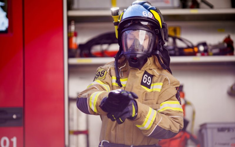 Photo of woman firefighter in helmet and mask standing near fire truck at fire station