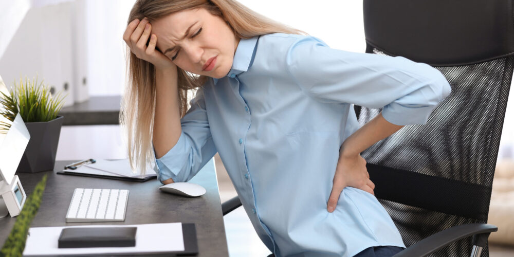 Young woman suffering from back pain in office